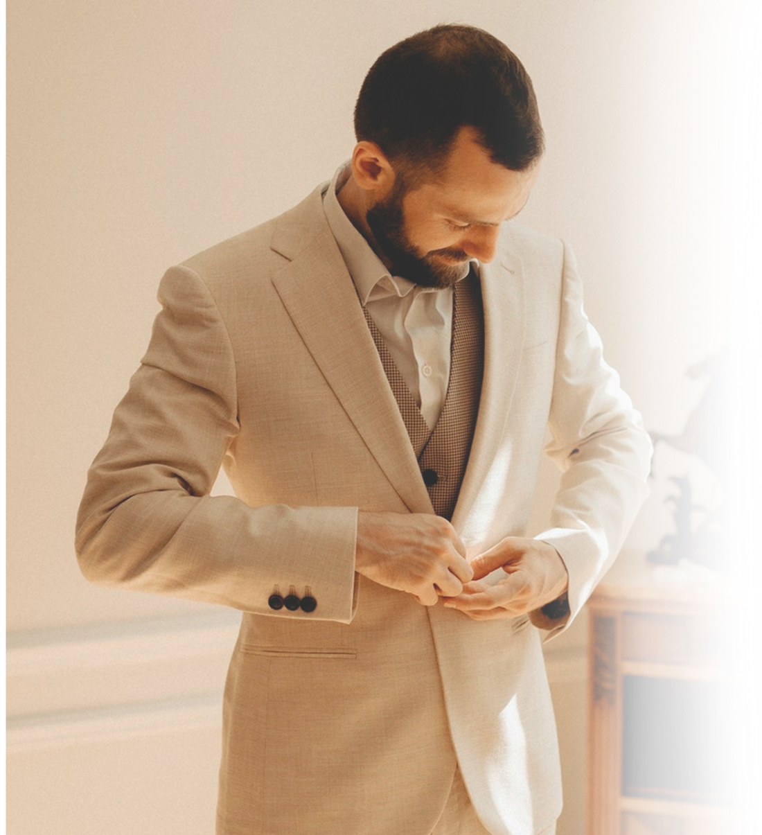 A man fastening a cream bespoke jacket worn over a brown waistcoat, made by Mr James in Playa del Rey