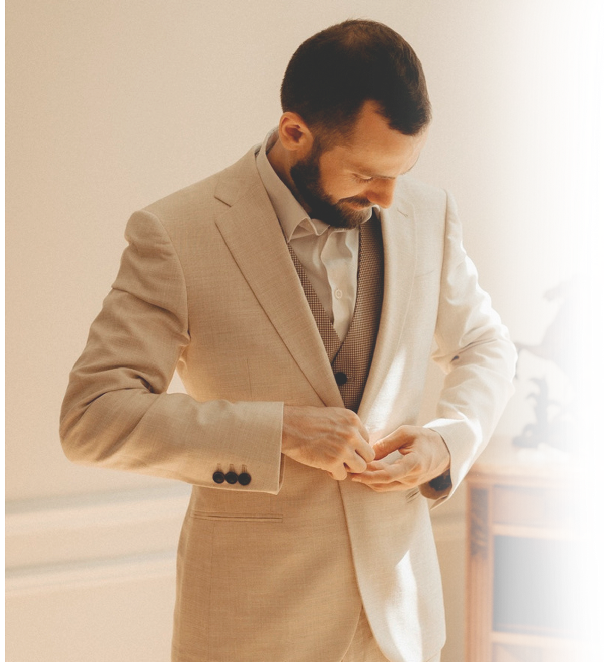 Man fastening a cream bespoke suit jacket worn over a brown waistcoat