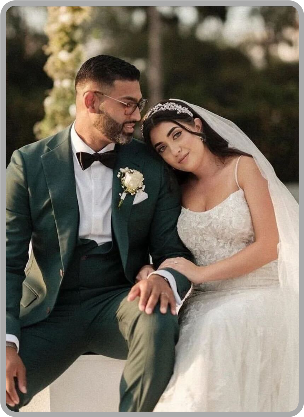 Groom in a dark green bespoke wedding suit seated beside his bride